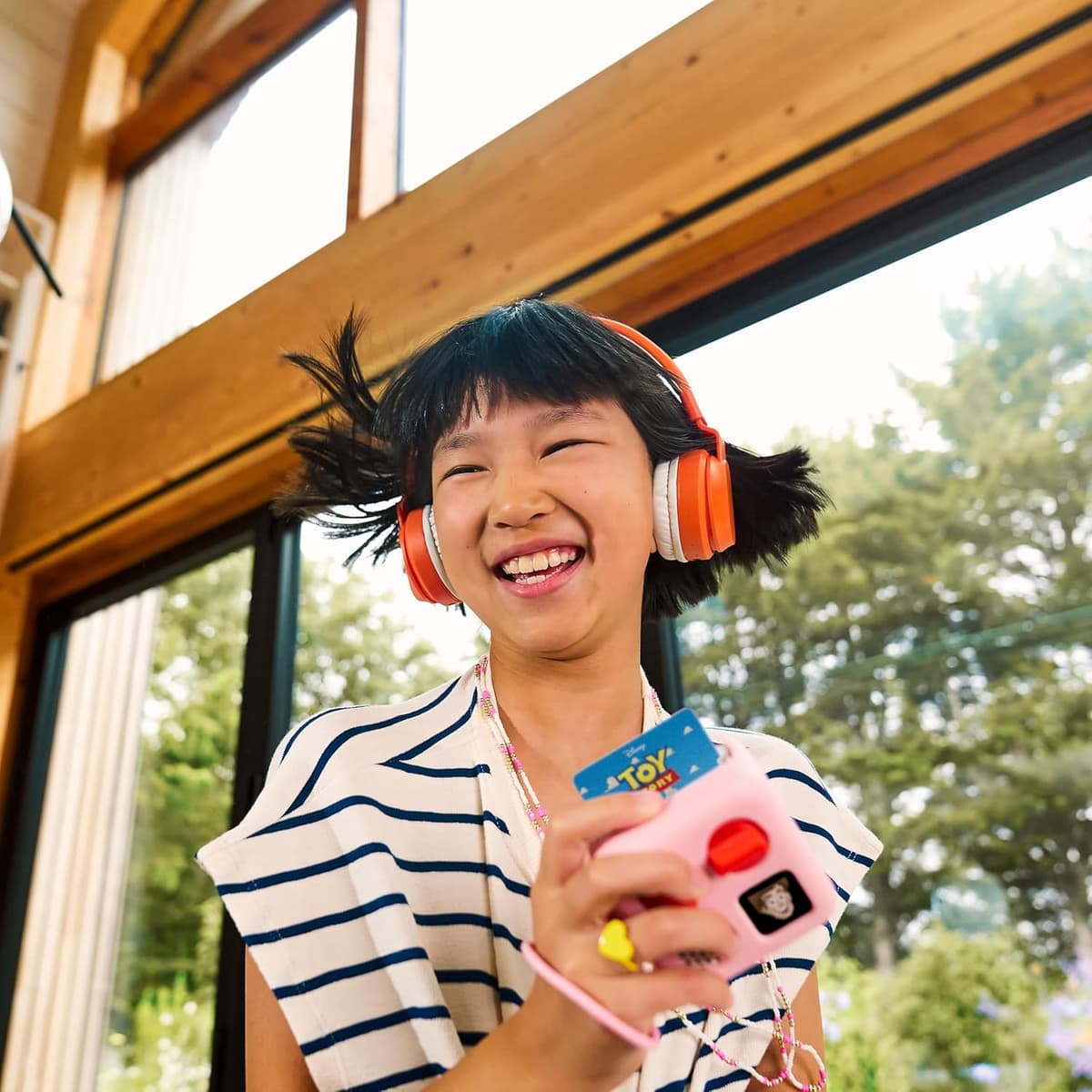 Child wearing orange headphones and holding a pink-jacketed Yoto Mini with a Toy Story card inserted